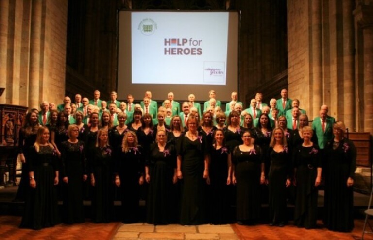Two choirs stood in front of a help for heroes image in the background.