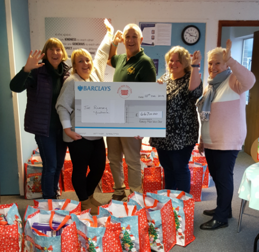 Group of adults holding a large cheque with xmas bags on the ground.